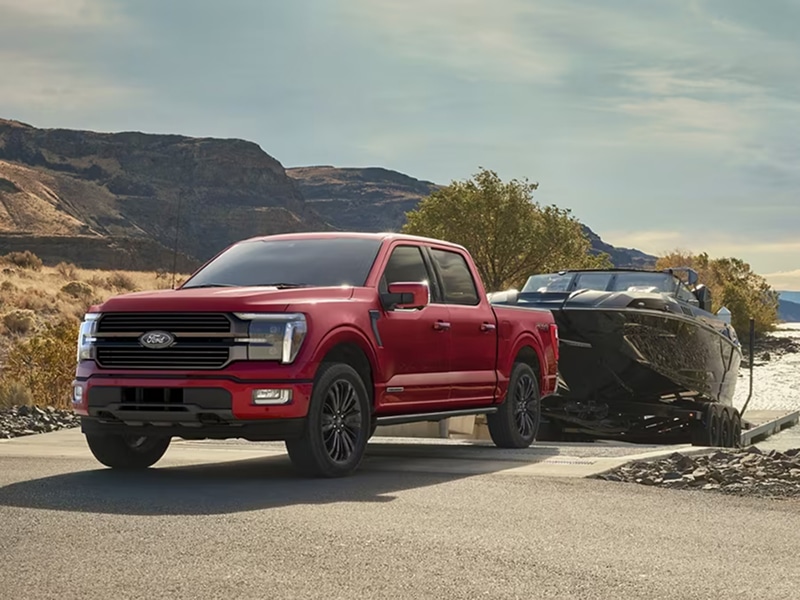 A red pickup truck towing a boat with a scenic desert landscape in the background.