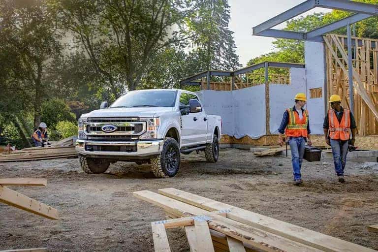White truck at a construction site with workers in hard hats and vests carrying equipment.