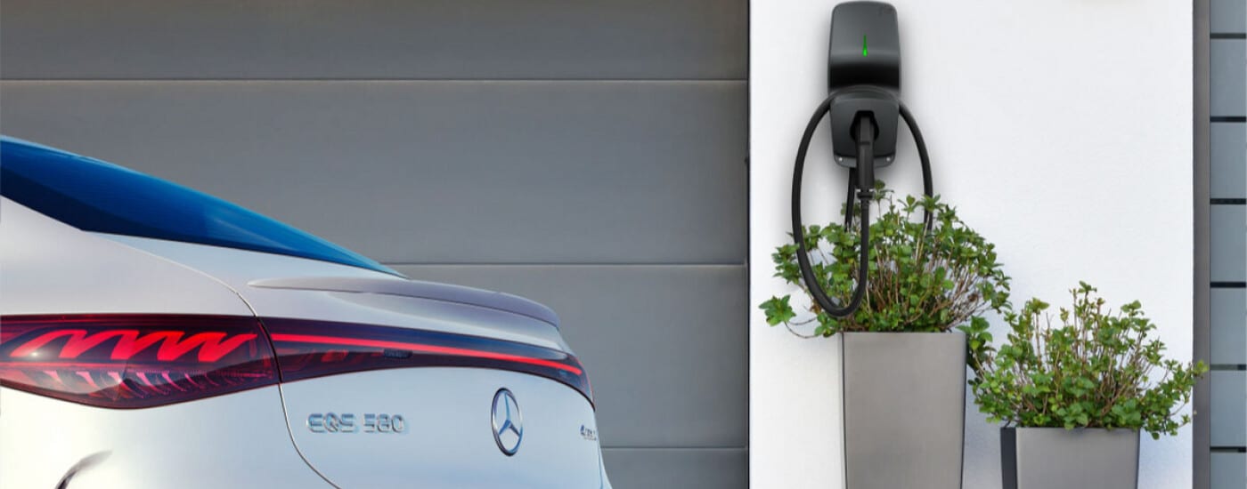 Electric car charging at home station, next to a white Mercedes-Benz EQS 580, near potted plants.