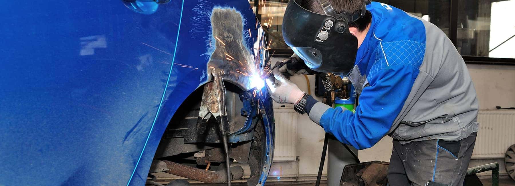 Mechanic welding car body in garage, wearing protective gear. Automotive repair service.