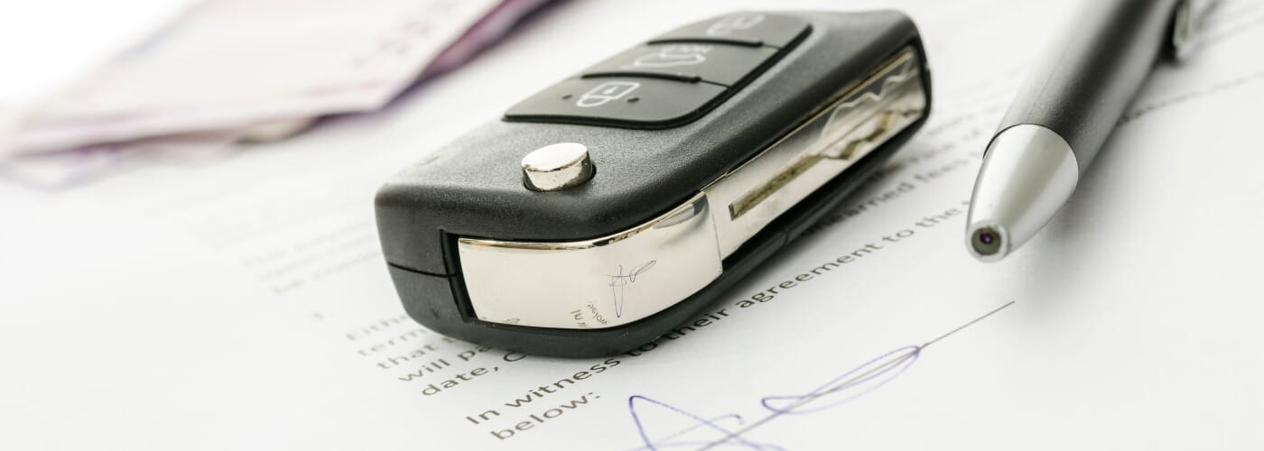 Car key and pen on a signed contract, highlighting vehicle agreement or purchase details.