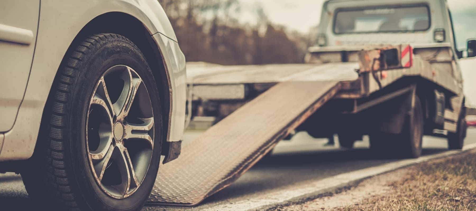 Car's front wheel near a towing truck ramp, suggesting roadside assistance.