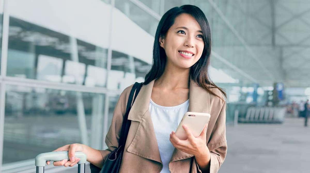 Woman smiling at airport with luggage and smartphone. Travel concept.