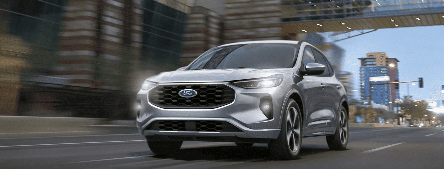 Silver Ford SUV driving through a city street with modern buildings in the background.