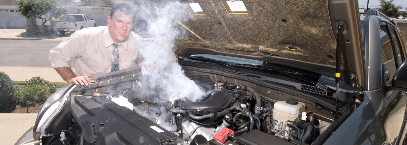 Man in a suit examines a smoking car engine on the street, showing signs of overheating.