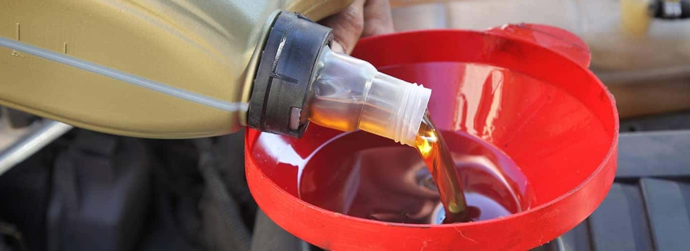 Pouring engine oil into a red funnel during a car maintenance session.