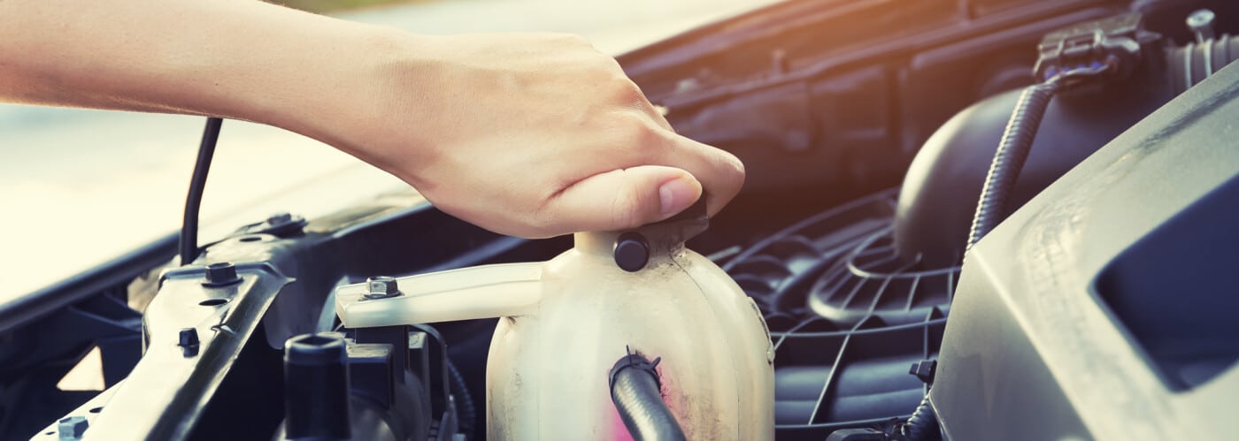 Hand adjusting coolant reservoir cap under car hood, highlighting automotive maintenance.