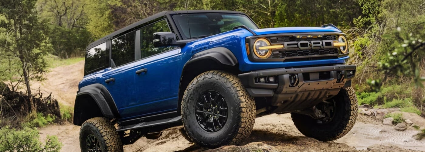 Blue Ford Bronco SUV off-roading on a rugged trail in a forested area.