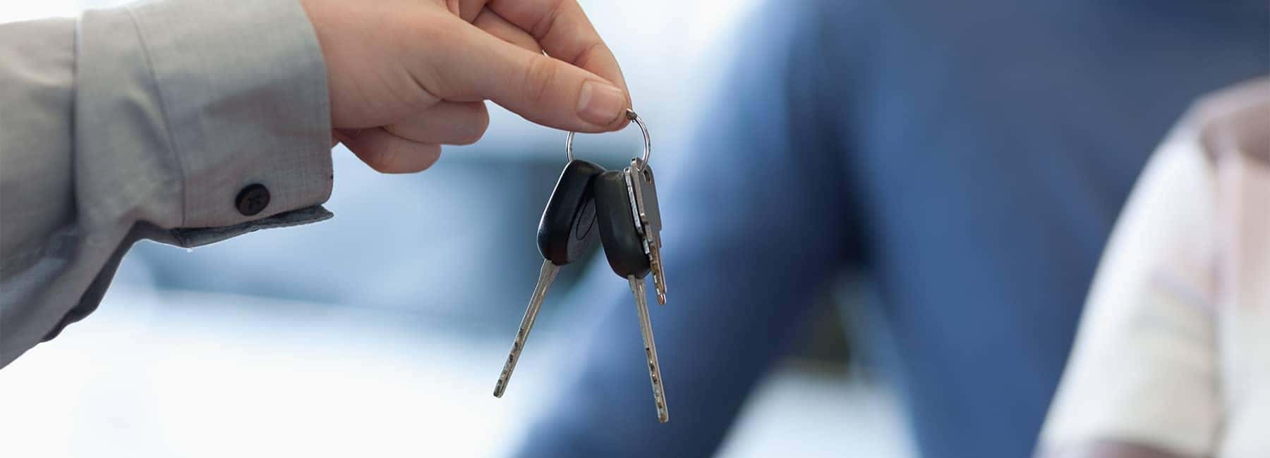 A person handing over car keys in an office setting, signifying ownership transfer.