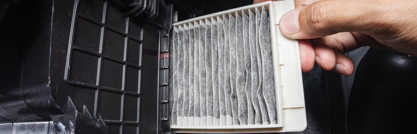Person replacing a car cabin air filter, showing the pleated design and hand positioning.