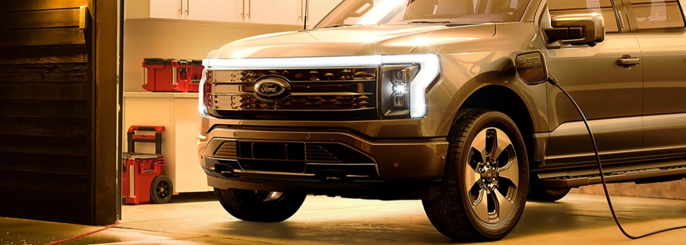 A Ford electric truck charging in a garage with toolboxes in the background.