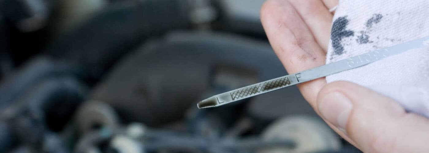 Person checking vehicle oil level with a dipstick, holding a cloth nearby.