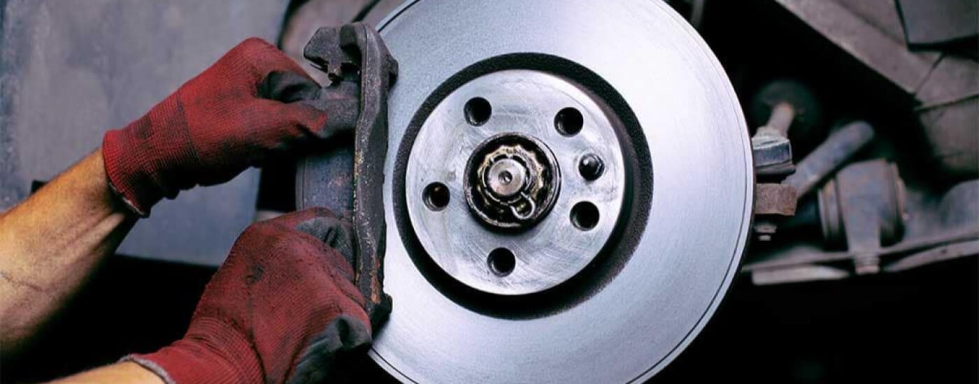 Mechanic adjusting a car brake disc with red gloves, highlighting vehicle maintenance.